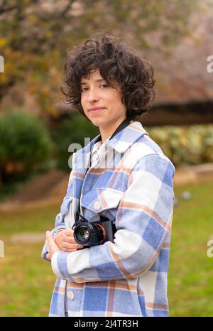 Junge Brünette Frau mit lockigen Haaren posiert mit ihrer Kamera Stockfoto