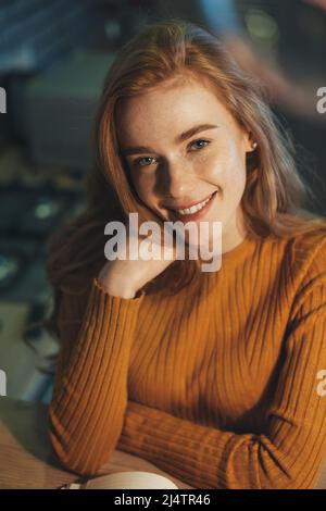 Glückliche Sommersprossen-Frau, die zu Hause sitzt, lernt, in ein Übungsbuch schreibt, lächelt. Porträt einer Geschäftsfrau. Moderner Lifestyle. Stockfoto