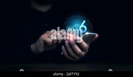 Das virtuelle Wi-Fi 6-Logo erschien auf dem mobilen Smartphone, während die Hand des Geschäftsmanns es auf dunklem Hintergrund verwendete. Telekommunikation der neuen Generation connectivi Stockfoto