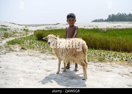 Bogra, Bangladesch. 20. März 2022. Ein Kind posiert für ein Porträt mit seinem Hausschaf am Ufer des Flusses Jamuna in Sariakandi Upazila des Bezirks Bogra. Kredit: SOPA Images Limited/Alamy Live Nachrichten Stockfoto