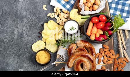 Bier- und Snackset. Oktoberfest Food Frame Konzept. Verschiedene Grillwürste, Bratkartoffeln, Pommes Frites, Gemüse, deutsches Brezelgebäck, Mandeln und Stockfoto