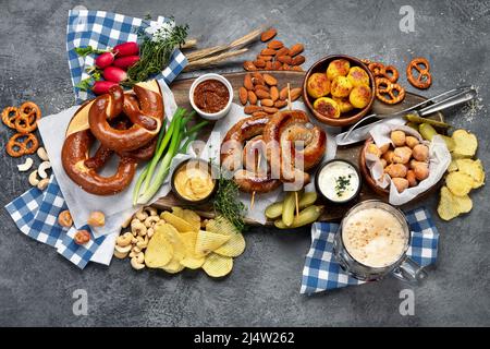 Oktoberfest Tischkonzept mit gegrillten Schweinswürsten, Brezelteig, Kartoffeln, Salat, Snacks, Saucen, Bier auf dunklem Hintergrund, Draufsicht. Stockfoto
