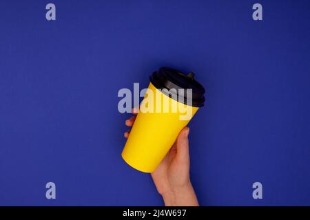 Papiertasse Kaffee in der Hand. Gelbe Papiertasse Kaffee in der Hand isoliert Nachbildung dunkelblauen Hintergrund Stockfoto