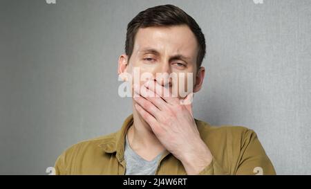 Junger Mann gähnt an der grauen Wand Stockfoto