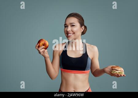 Frau, die zwischen Apfel und Hamburger wählen kann. Diät-Konzept. Stockfoto