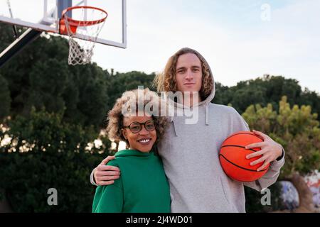 die lateinerin und der kaukasische Mann posieren lächelnd auf dem Basketballplatz in einem Stadtpark, Konzept der Freundschaft und des städtischen Sports Stockfoto