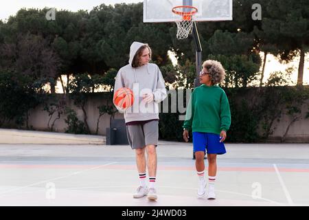 lateinische Frau und kaukasischer Mann plaudern beim Gehen auf dem Basketballplatz nach einem Spiel, Konzept der Freundschaft und städtischen Sport auf der Straße, Kopie s Stockfoto