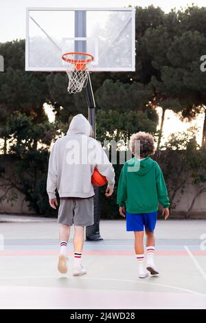 Rückansicht einer latinerin und eines kaukasischen Mannes, die nach dem Basketballtraining, dem Konzept der Freundschaft und dem urbanen Sport in der Straße den Platz hinunter plaudern Stockfoto