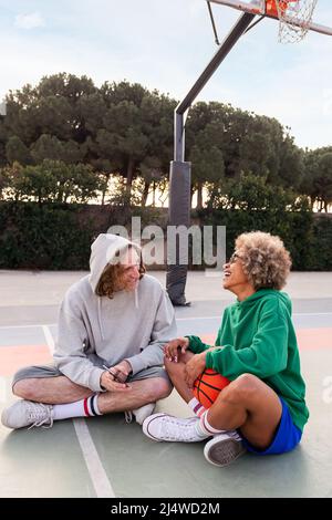 Mann und Frau lachen und Spaß mit dem Telefon nach dem Basketball-Training in einem Stadtpark, Konzept der Freundschaft und städtischen Sport auf der Straße, Co Stockfoto