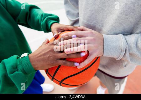 Verbunden Hände eines kaukasischen Mannes und einer lateinischen Frau über einen Basketball, Konzept der Freundschaft und städtischen Sport auf der Straße, kopieren Raum für Text Stockfoto