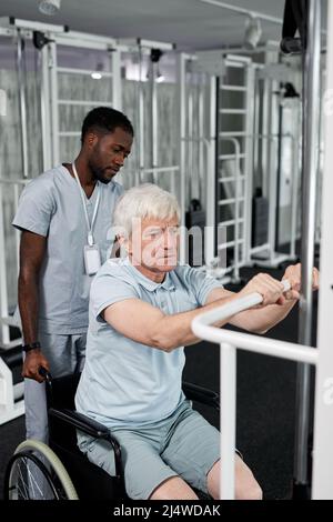 Porträt eines älteren Mannes, der im Fitnessstudio einen Rollstuhl benutzt und Rehabilitationsübungen macht Stockfoto