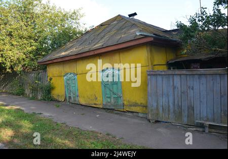 Ein sehr altes kleines Haus mit gelben Wänden und grünen Holzfensterläden, die auf einer viel niedrigeren Ebene als die Straße stehen. Stockfoto