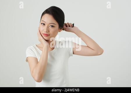 Porträt einer jungen asiatischen Frau, die Haare verdreht und ihr Gesicht berührt Stockfoto