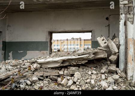 Blick durch das zerstörte Fenster von Wohngebäuden mit einem Haufen grauer Betonschutt im Vordergrund. Hintergrund. Stockfoto