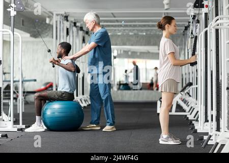 Ganzkörperportrait von Menschen, die Physiotherapie-Geräte im Fitnessstudio in der Rehabilitationsklinik verwenden Stockfoto