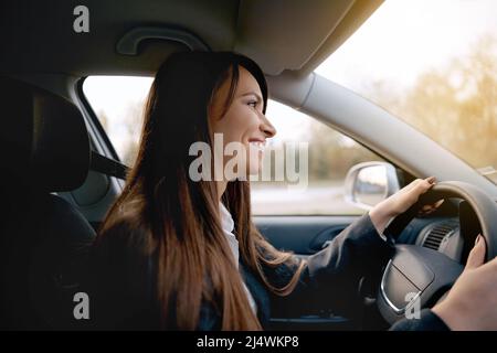 Schöne junge glücklich lächelnde Frau, die ihr neues Auto fährt Stockfoto