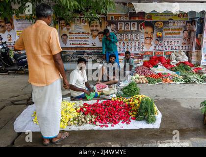 Männer, die auf dem Bürgersteig sitzen und Blumenköpfe und Gemüse in Trichy, Tamil Nadu, Indien, verkaufen Stockfoto