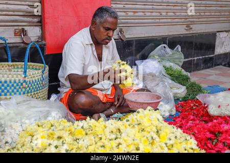 Mann, der auf dem Bürgersteig sitzt und die Blumenköpfe nach Gewicht in Trichy, Tamil Nadu, Indien verkauft Stockfoto