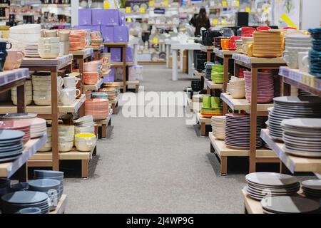 Gerichte werden im Laden verkauft. Reihen von verschiedenen bunten Tassen, Schüsseln und Tellern für zu Hause auf Regalen in einem Supermarkt. Stockfoto