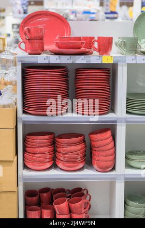 Gerichte werden im Laden verkauft. Reihen von verschiedenen roten Tassen, Schüsseln und Tellern für Zuhause auf Regalen in einem Supermarkt. Stockfoto