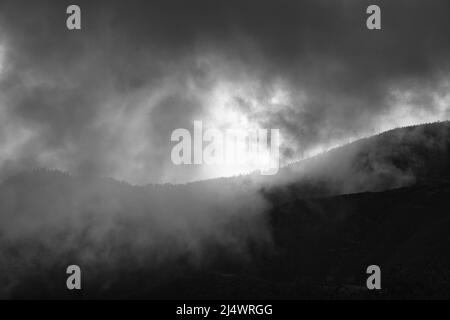 Ein Schwarz-Weiß-Bild vom Berg hinunter durch die Wolken bis zum strahlenden atlantik. Madeira-Inseln, Portugal Stockfoto