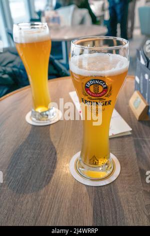 Cuxhaven, Deutschland - 02.25.2022: Zwei schlanke, hohe Brillen o Erdinger Weissbier auf einem kleinen runden Tisch im Innenbereich Stockfoto