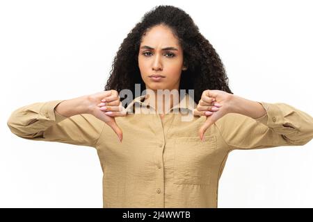 Verärgert junge afroamerikanische Frau, die Ablehnung und Negativ zeigt, mit Daumen nach unten Geste isoliert auf Weiß. Die traurige Dame zeigt eine widerwillige, schlechte Kritik, eine Geste, die nicht gefällt Stockfoto