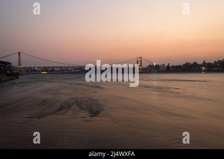 Eisen Hängebrücke mit Sonnenuntergang dramatischen Himmel und verschwommen fließenden Flusswasser am Abend Bild wird in rishikesh uttrakhand indien aufgenommen. Stockfoto