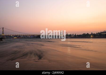 Eisen Hängebrücke mit Sonnenuntergang dramatischen Himmel und verschwommen fließenden Flusswasser am Abend Bild wird in rishikesh uttrakhand indien aufgenommen. Stockfoto