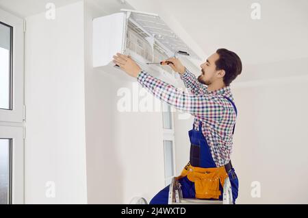 Junger Techniker, der einen Schraubendreher verwendet, während er eine Klimaanlage an der Wand repariert Stockfoto