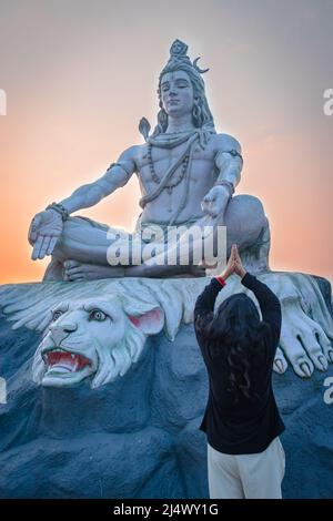 Mädchen beten an hindu gott herr shiva Statue in Meditationshaltung mit dramatischen Himmel am Abend Bild wird am Parmarth niketan rishikesh uttrakhand genommen Stockfoto