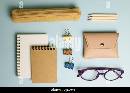 Notizblock, Clip, Bleistift, Tasche, Etui, Brille auf blauem Hintergrund. Flach liegend, Draufsicht Stockfoto