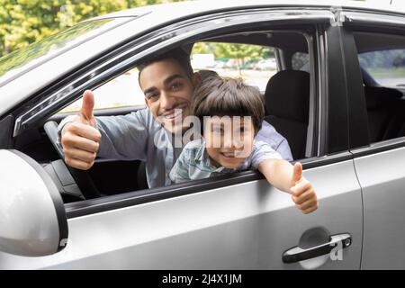 Froh glücklich Millennial araber Kerl lehrt kleinen Jungen Auto zu fahren, Vater und Sohn zeigen Daumen nach oben in offenem Fenster Stockfoto