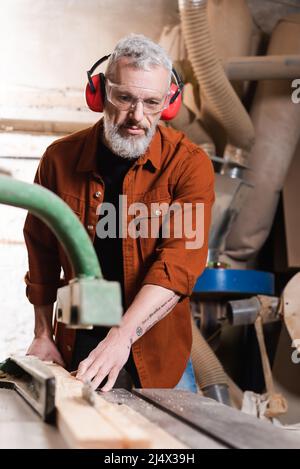 Zimmermann mittleren Alters, der in der Werkstatt an einer verschwommenen Jointer-Maschine arbeitet Stockfoto