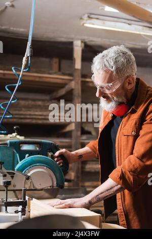 Tätowierte Tischlerei in Brillen Sägen von Holz im Holzwerkstudio Stockfoto