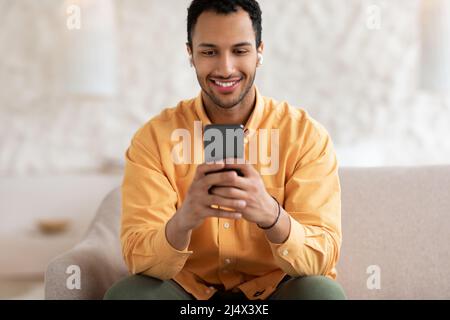 Glücklicher arabischer Mann, der Kopfhörer mit dem Handy trägt Stockfoto