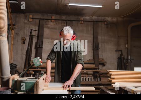 Glücklicher Zimmermann mittleren Alters, der in der Werkstatt an einer Jointer-Maschine arbeitet Stockfoto