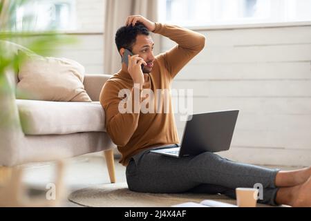 Verwirrter arabischer Mann, der mit einem Laptop auf dem Mobiltelefon spricht Stockfoto