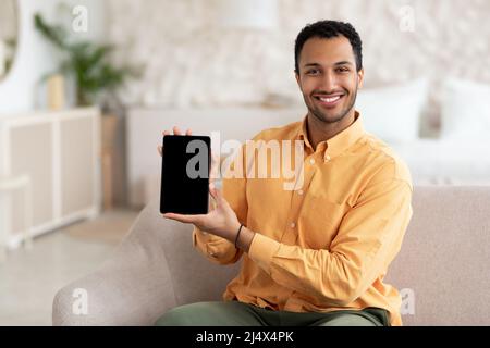 Lächelnder junger arabischer Mann, der ein digitales Tablet mit leerem Bildschirm zeigt Stockfoto
