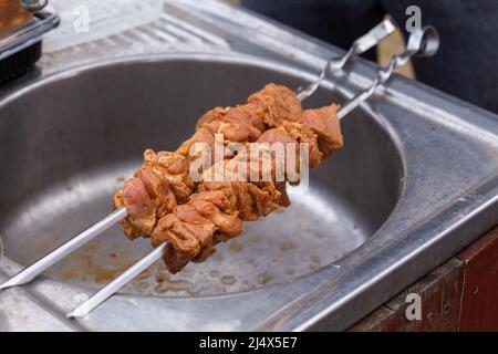 Saftiger Shish Grill aus frischem Fleisch auf Spieße zum Kochen auf dem Grill. Rohes Fleisch wird auf dem Grill aufgereiht. Shashlik ist bereit zu kochen Stockfoto