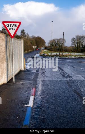 Rot, weiß und blau gestrichene Bordsteine und ein Wegweiser im Dorf Ballybogey. In der Ferne ein rotes Auto und ein weißes Auto weg Fr. Stockfoto