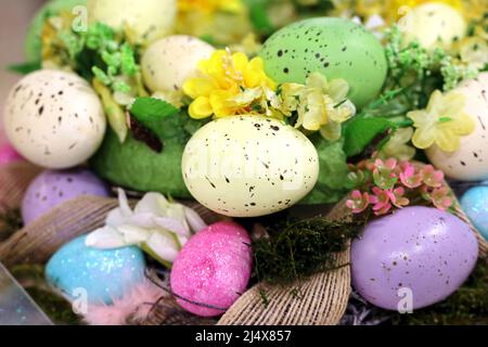 Ostereier und künstliche Blumen im Weidenkorb. Bunte Dekorationen, festlicher Hintergrund Stockfoto