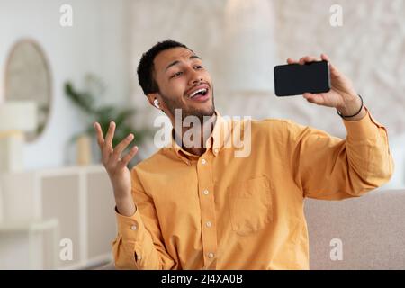 Glücklicher arabischer Mann, der mit einem Mobiltelefon Kopfhörer trug und sang Stockfoto