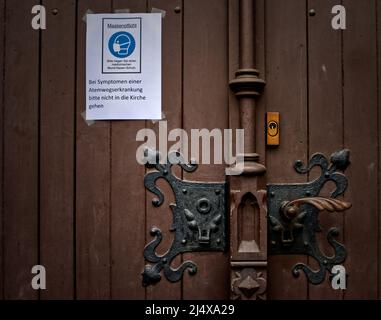 schild für obligatorische Gesichtsmasken und Warnung, bei Symptomen einer Atemwegserkrankung nicht in die Kirche zu gehen, an einer schweren braunen Holztür (in Deutschland) Stockfoto