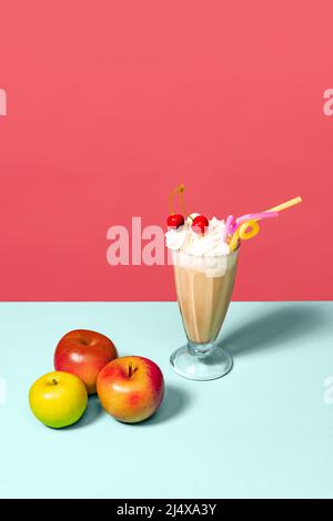 Irischer Kaffee und Äpfel. Hohes Glas mit Milchcocktail isoliert auf hellrosa Hintergrund. Trendige Farben. Pop-Art, Retro-Style. Stockfoto