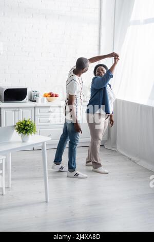 In voller Länge ein glückliches afroamerikanisches Senioren-Paar, das in der Küche tanzt Stockfoto