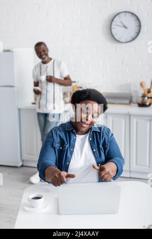 Glückliche afroamerikanische Frau, die während eines Videoanrufs spricht, fast verschwommener Ehemann Stockfoto