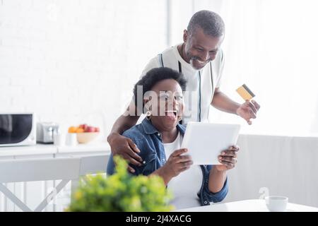 Senior african american Mann mit Kreditkarte in der Nähe erstaunt Frau mit digitalen Tablet Stockfoto