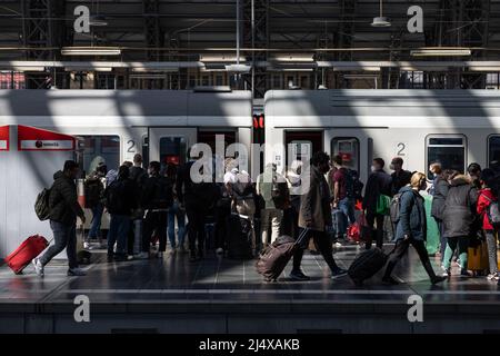 18. April 2022, Hessen, Frankfurt/Main: Reisende mit Gepäck steigen in einen Zug ein oder gehen am Frankfurter Hauptbahnhof entlang des Bahnsteigs. An besonders stark frequentierten Hauptbahnhöfen stehen zusätzliche Mitarbeiter am Osterwochenende und am Ostermontag zur Verfügung, um den Gästen beim Wechsel von Zügen und beim ein- und anderen Bahnsteigen zu helfen. Foto: Hannes Albert/dpa Stockfoto