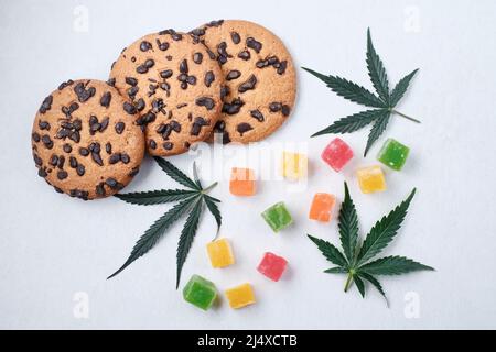 Amerikanische Cookies mit Cannabisextrakt. Süßigkeiten mit CBD-Öl. Marihuana Blätter auf weißem Hintergrund. Draufsicht, flach liegend. Stockfoto